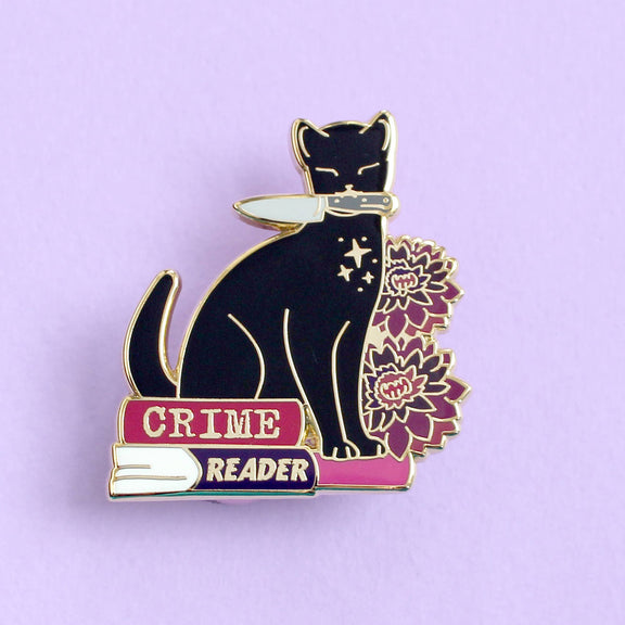 Pin's Glitter Punk Crime Reader, chat noir avec couteau assis sur une pile de polars et fleurs pourpres