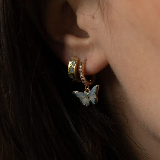Boucles d'oreilles huggie dorées Fable England, charm papillon bleu émaillé à la main et zircones