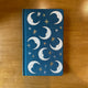 Carnet relié Designworks Ink à couverture en tissu bleu profond ornée de lunes et d'étoiles dorées