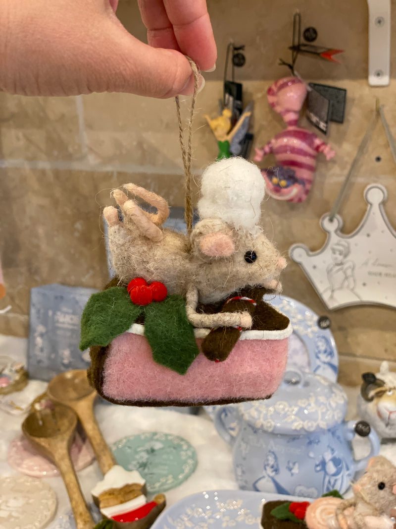 Souris pâtissière en laine feutrée à suspendre, posée sur une part de gâteau rose avec houx