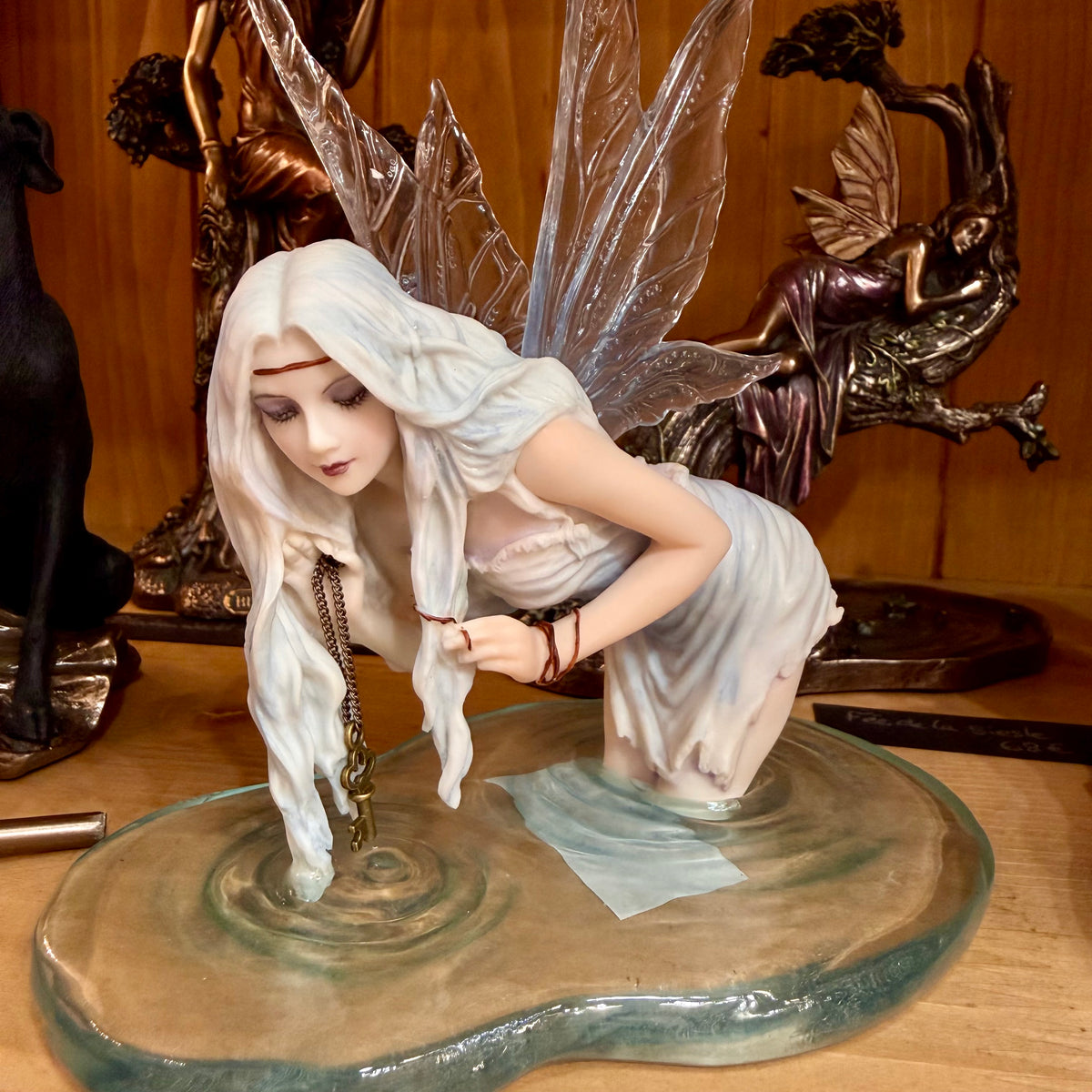 Statuette fée des eaux agenouillée dans une flaque bleue tenant une clé dorée, ailes translucides