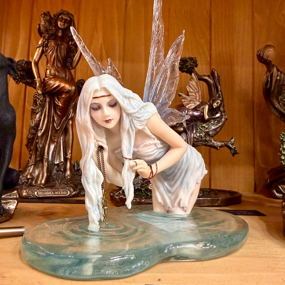 Statuette fée des eaux agenouillée dans une flaque bleue tenant une clé dorée, ailes translucides