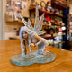 Statuette fée des eaux agenouillée dans une flaque bleue tenant une clé dorée, ailes translucides