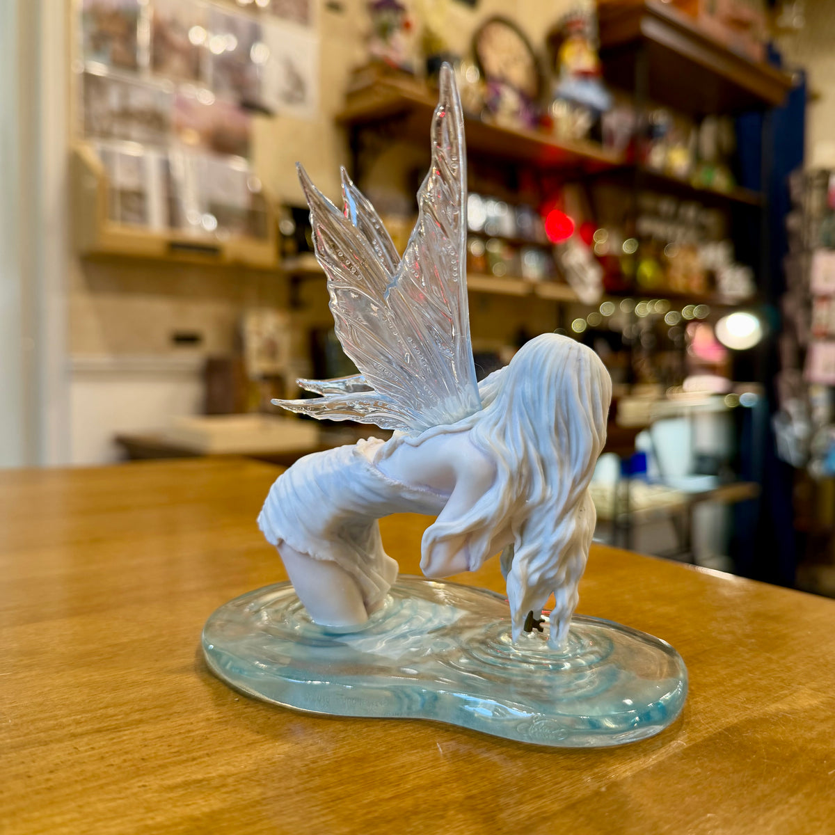 Statuette fée des eaux agenouillée dans une flaque bleue tenant une clé dorée, ailes translucides
