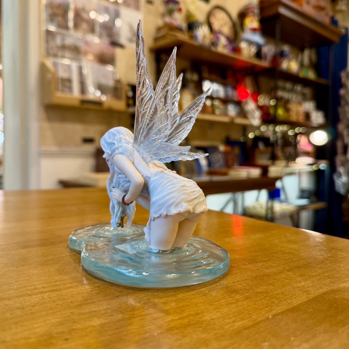 Statuette fée des eaux agenouillée dans une flaque bleue tenant une clé dorée, ailes translucides