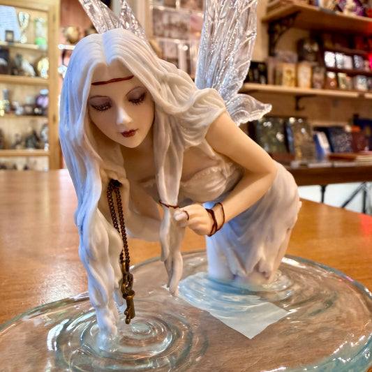 Statuette fée des eaux agenouillée dans une flaque bleue tenant une clé dorée, ailes translucides