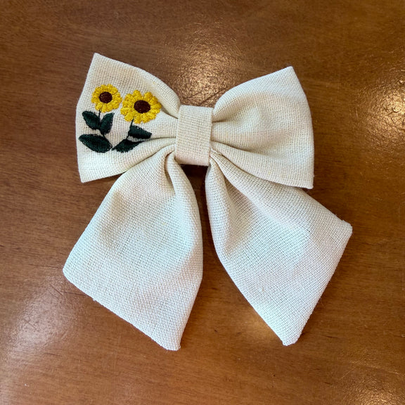 Pince à cheveux nœud en tissu écru texturé brodé d'un tournesol jaune, format compact