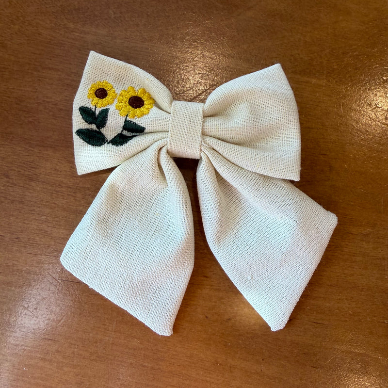 Pince à cheveux nœud en tissu écru texturé brodé d'un tournesol jaune, format compact