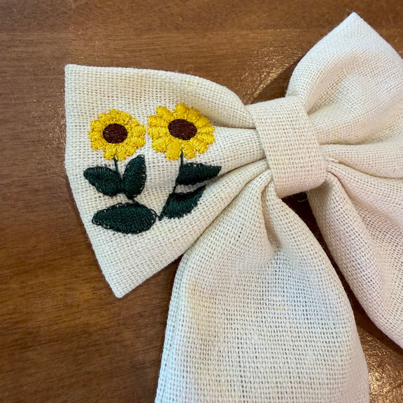Pince à cheveux nœud en tissu écru texturé brodé d'un tournesol jaune, format compact