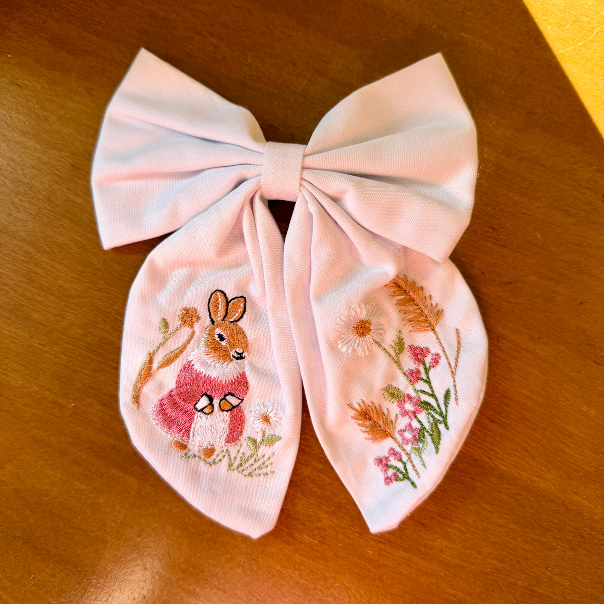 Pince à cheveux nœud en tissu blanc texturé brodé d'un petit lapin entouré de fleurs printanières