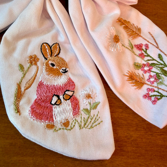 Pince à cheveux nœud en tissu blanc texturé brodé d'un petit lapin entouré de fleurs printanières