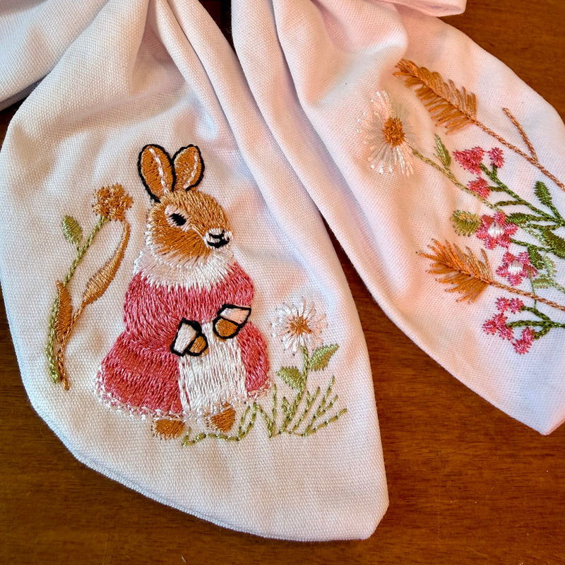 Pince à cheveux nœud en tissu blanc texturé brodé d'un petit lapin entouré de fleurs printanières