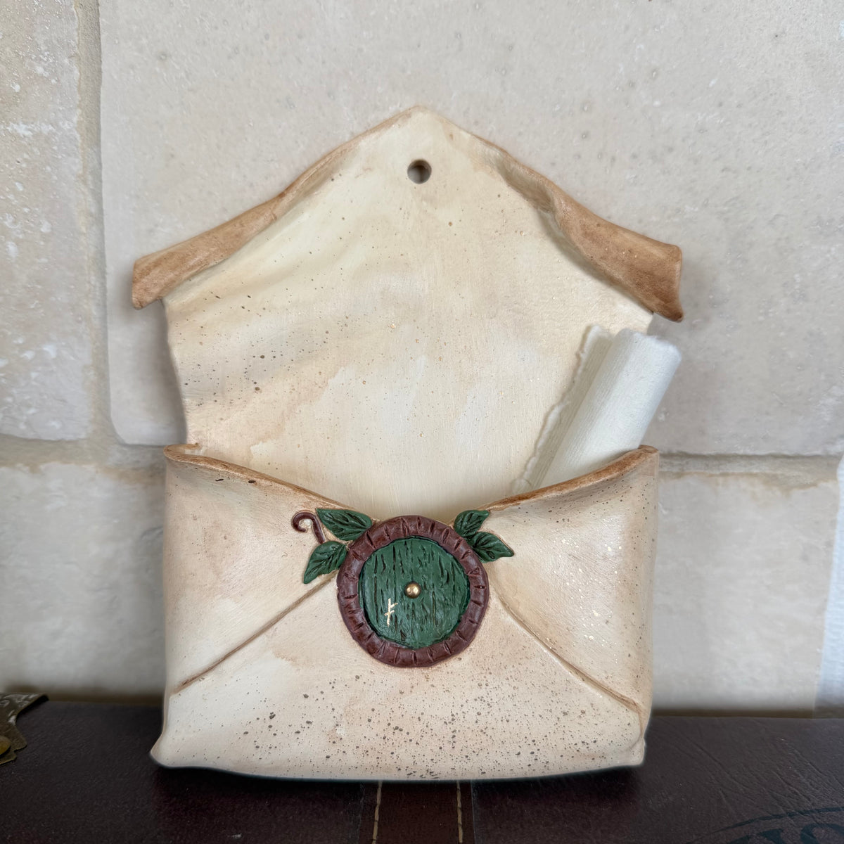 Enveloppe murale artisanale en argile effet vieux parchemin ornée d'une petite porte ronde de maison hobbit