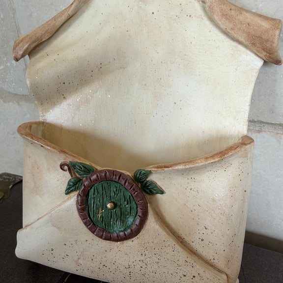 Enveloppe murale artisanale en argile effet vieux parchemin ornée d'une petite porte ronde de maison hobbit