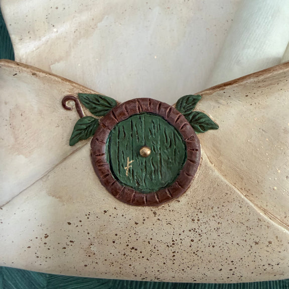 Enveloppe murale artisanale en argile effet vieux parchemin ornée d'une petite porte ronde de maison hobbit