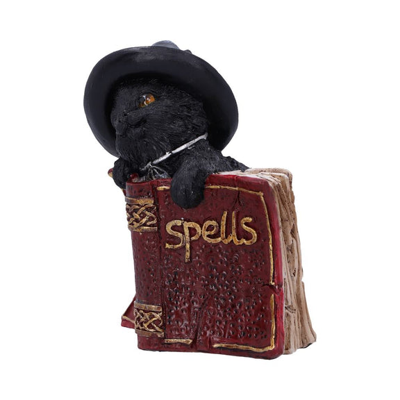 Statuette en résine d'un chat noir coiffé d'un chapeau de sorcier derrière un livre de sortilèges rouge