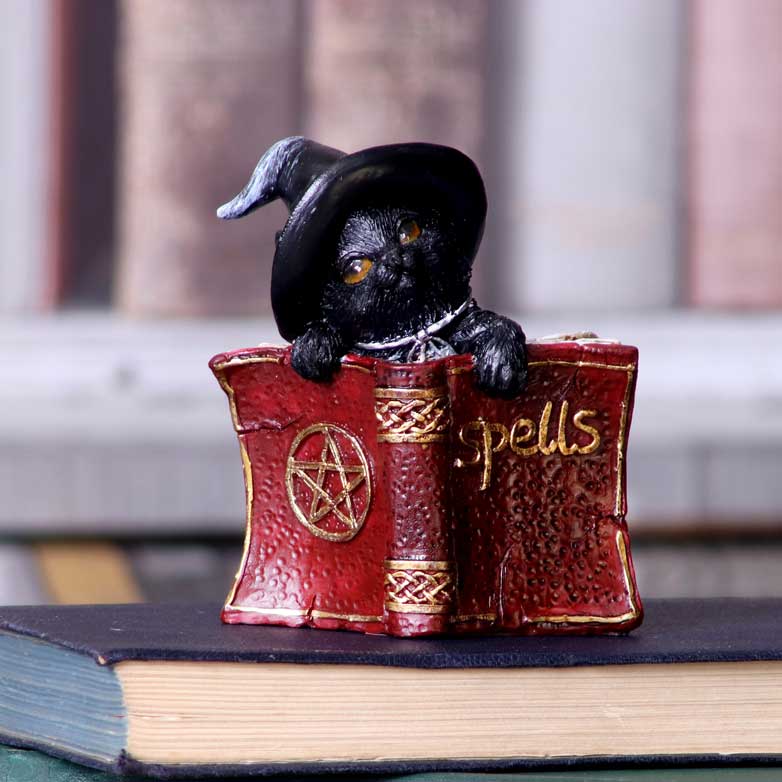 Statuette en résine d'un chat noir coiffé d'un chapeau de sorcier derrière un livre de sortilèges rouge