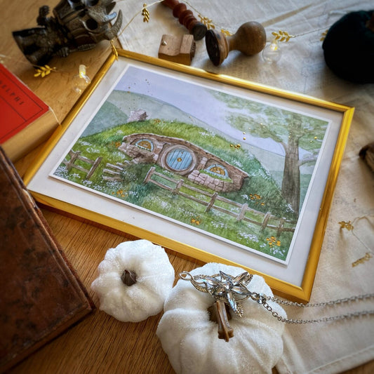 Illustration A5 d'une maison de hobbit à porte ronde et toit végétalisé nichée dans les collines verdoyantes